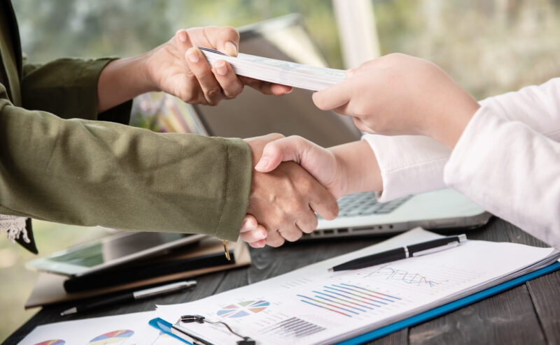 Business people shaking hands, finishing up meeting. businessman giving money to his partner while making contract - bribery and corruption concepts.