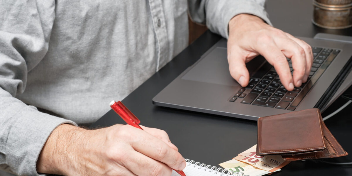 Close-up of a businessman or accountant holding pen working at desk using a laptop to calculate financial report or tax payments. Business concept of accounting, paying taxes, calculating finances