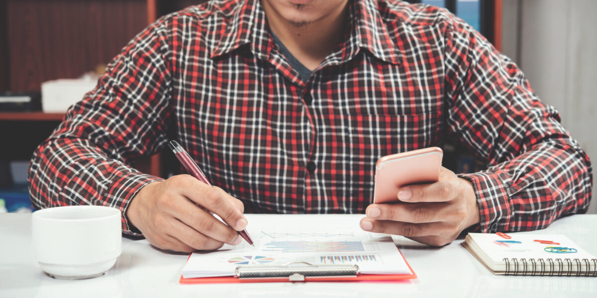 Close up young man working and smart phone and laptop on wooden desk in office