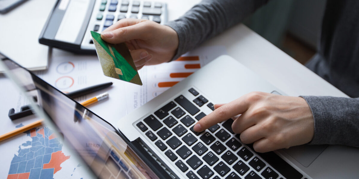 Cropped view of business person working on laptop computer, holding credit card and doing online banking