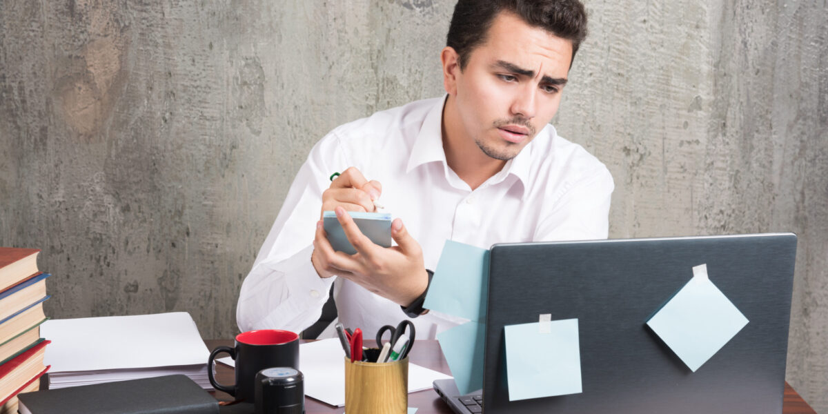Office employee looking at laptop and holding telephone at the office desk. High quality photo